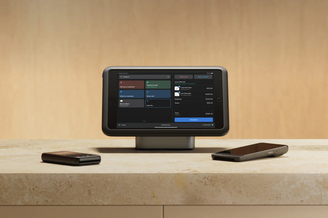 Shopify POS on a countertop with two payment terminals beside it, against a beige wall.